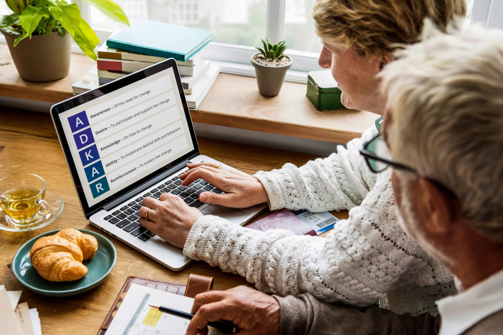 Two people looking at a screen displaying the ADKAR acronym of change management - Awareness, Desire, Knowledge, Ability and Reinforcement.